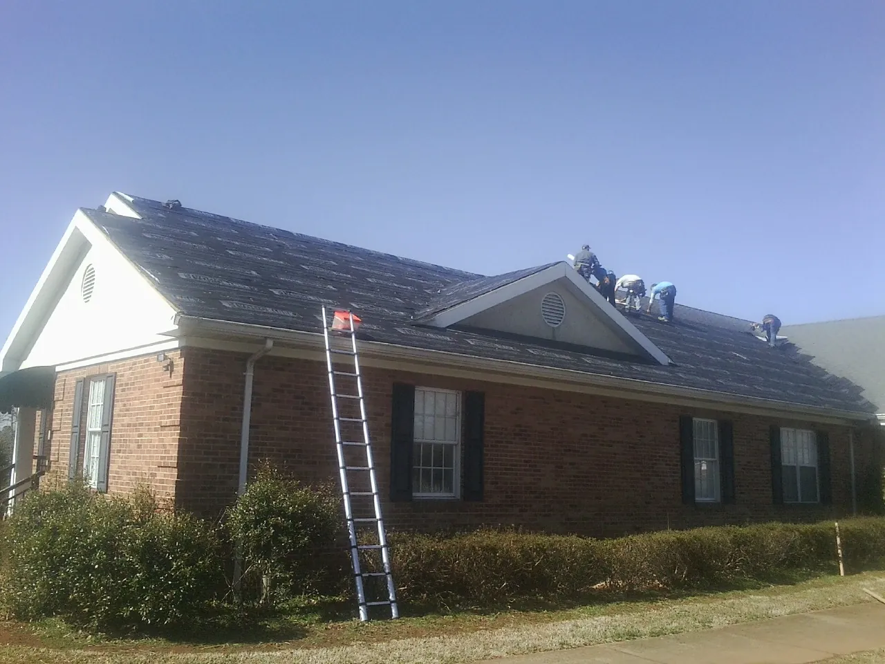 Crew tearing shingles off a brick ranch roof with a ladder set — Emergency Roof Repair work by our crew in New Egypt