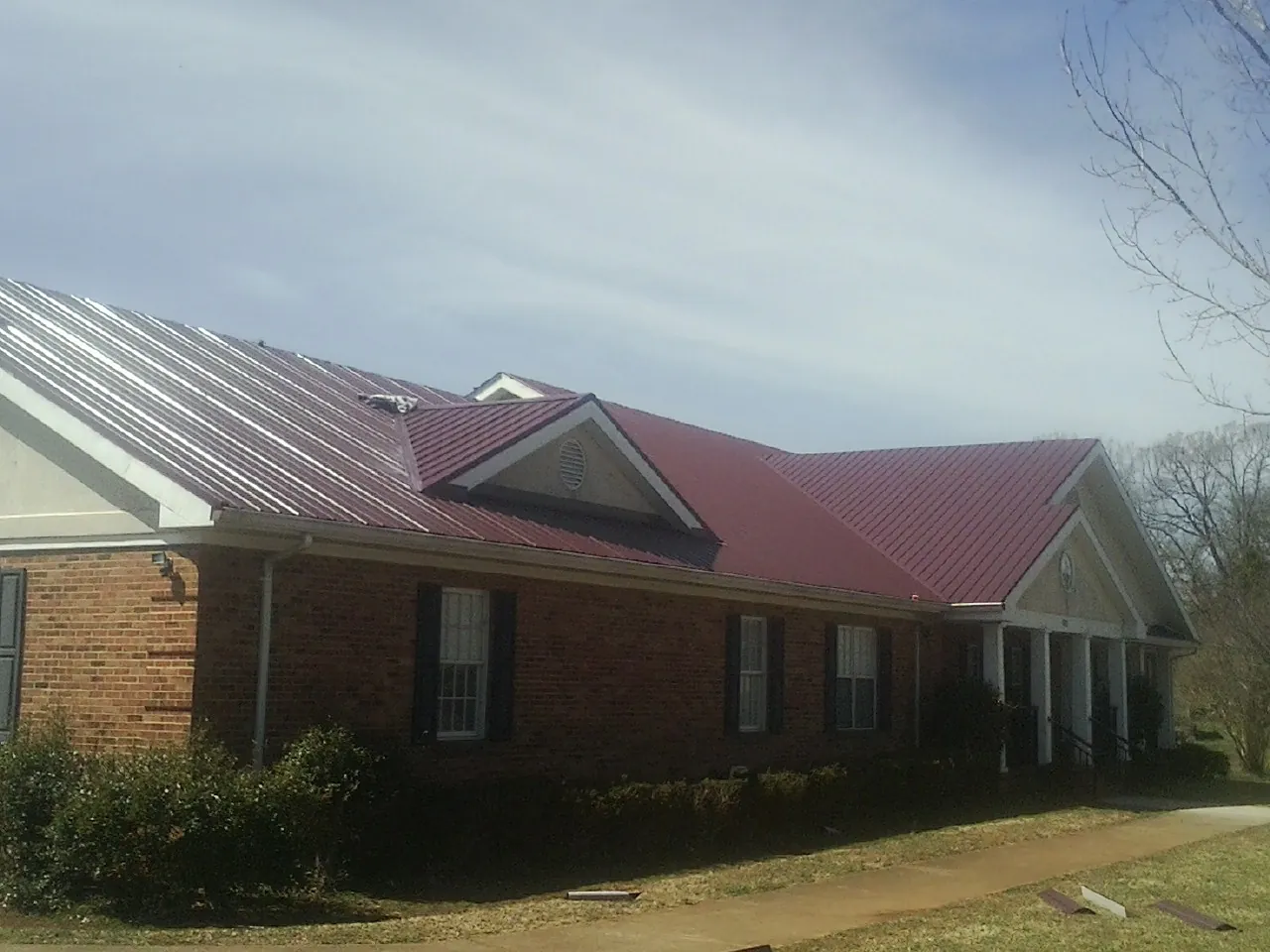 Red metal roof with gabled entries on a long brick building, from a Hail Damage Roof Repair job in New Egypt