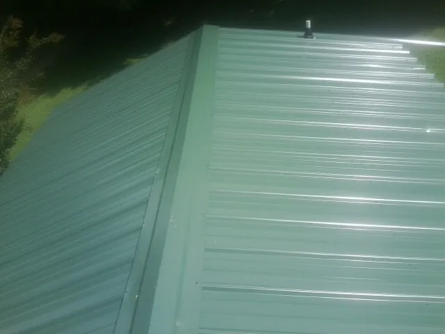 New green metal panels meeting at the ridge of a roof — Flat Roof Repair work by our crew in New Egypt