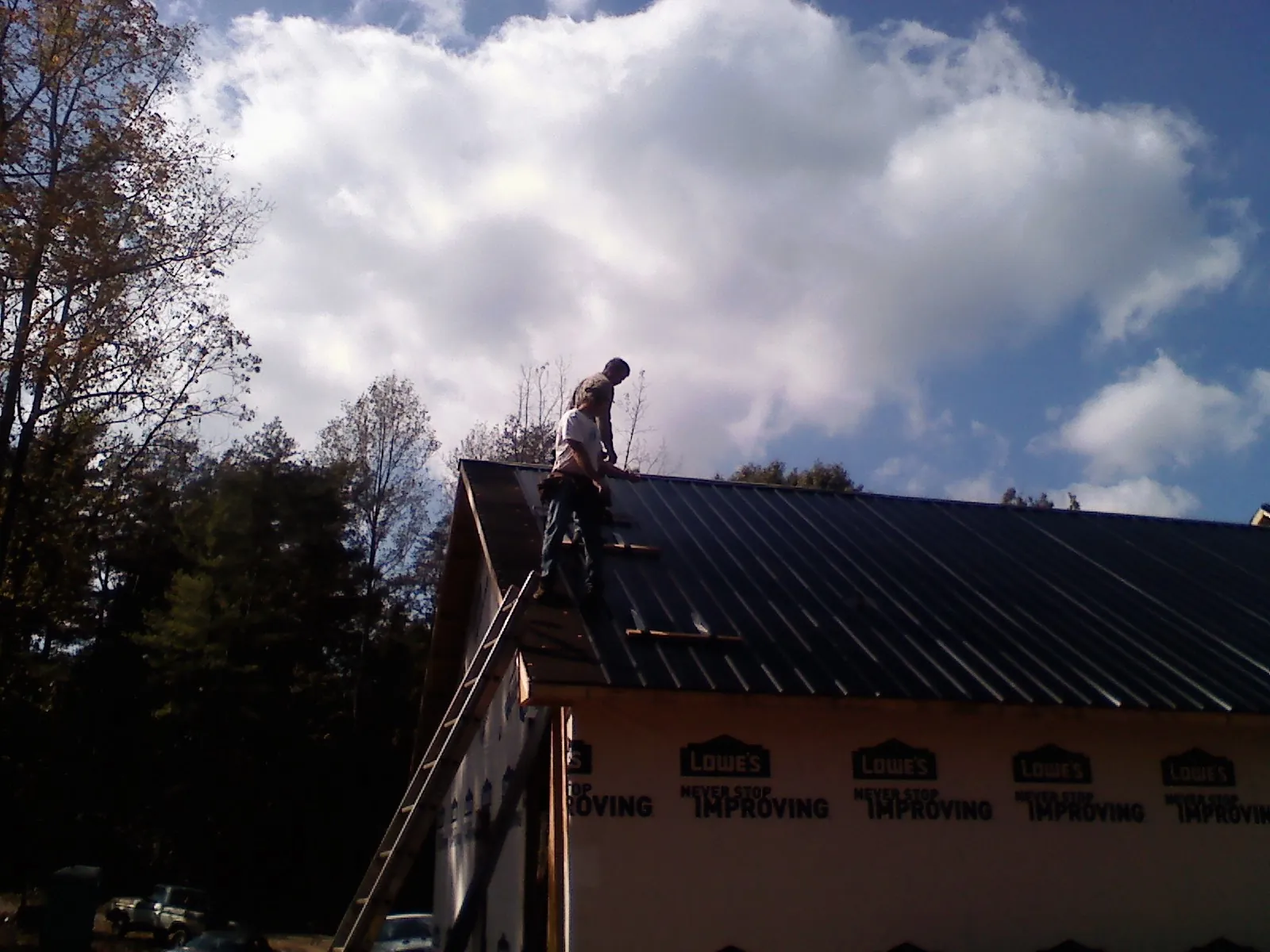 Roofer fastening dark metal panels high against a cloudy sky, from a Roof Inspection job in New Egypt