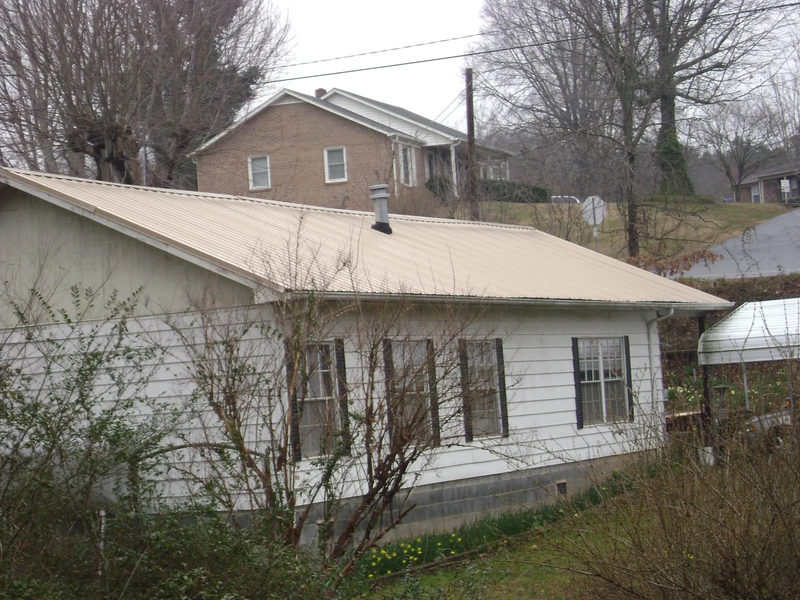 Tan metal roof on a white sided house set into a hillside — Commercial Roofing by Roofing Brothers in New Egypt