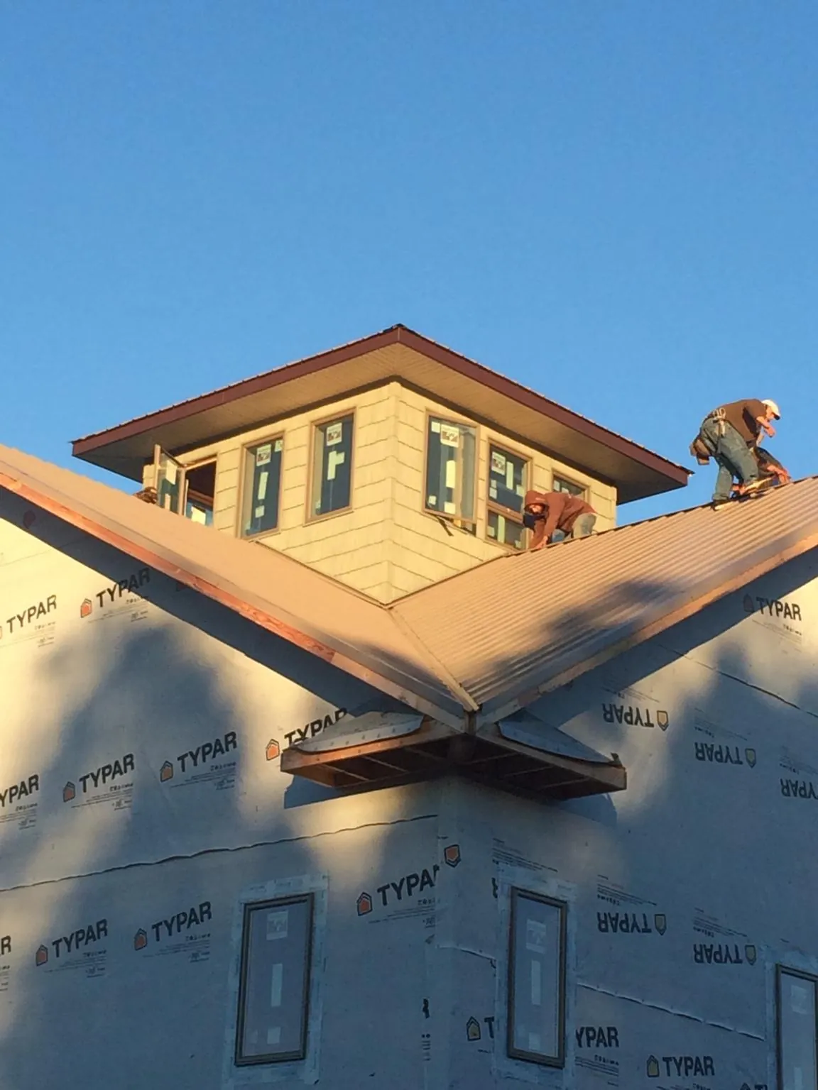 Roofers working around a rooftop cupola on a new metal roof at sunset in New Egypt